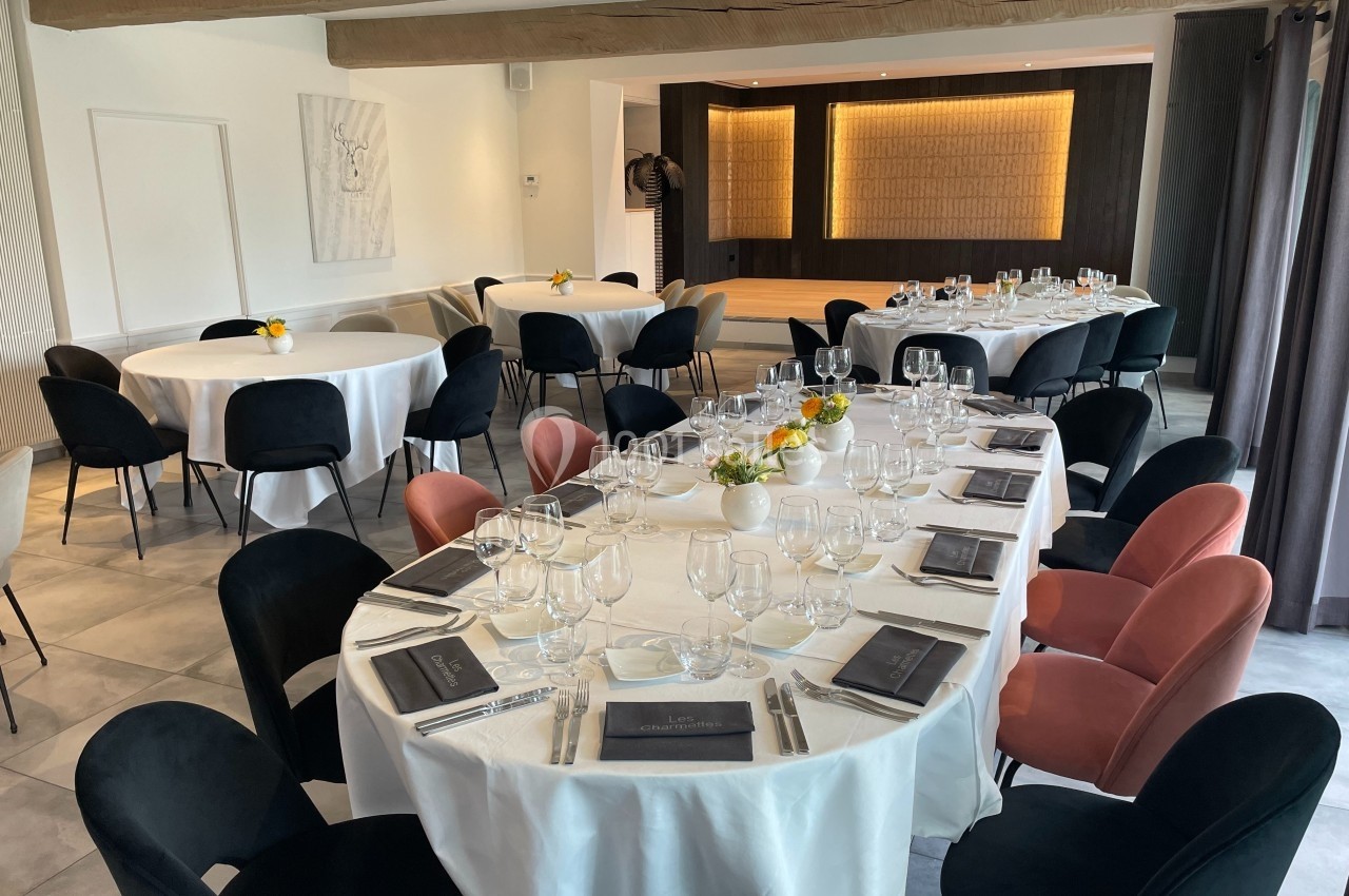 Salle de réception lumineuse avec tables rondes et rectangulaires dressées, décorée de fleurs et chaises colorées.