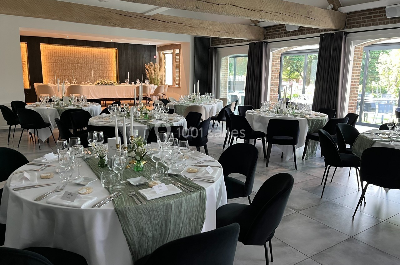 Salle de réception élégante avec tables rondes dressées, nappes blanches et décorations vertes, éclairage naturel.