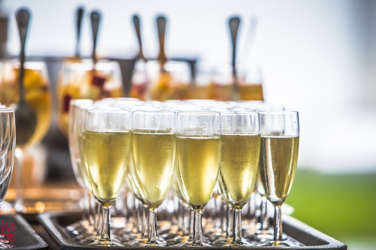 Flûtes de champagne alignées sur une table, avec des verrines de fruits en arrière-plan.
