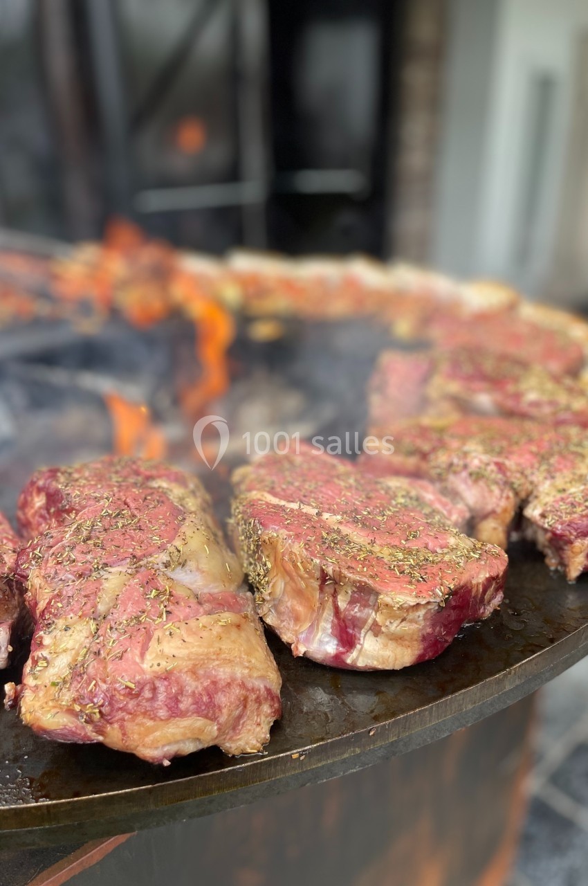 Viande rouge assaisonnée en train de griller sur une plaque chauffante au-dessus d'un feu de bois.