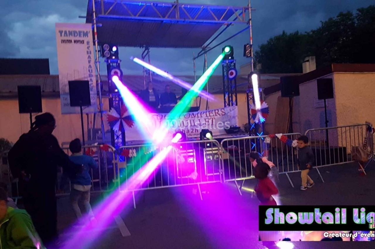 Scène extérieure avec éclairages colorés, enfants jouant au premier plan et structures métalliques en arrière-plan.