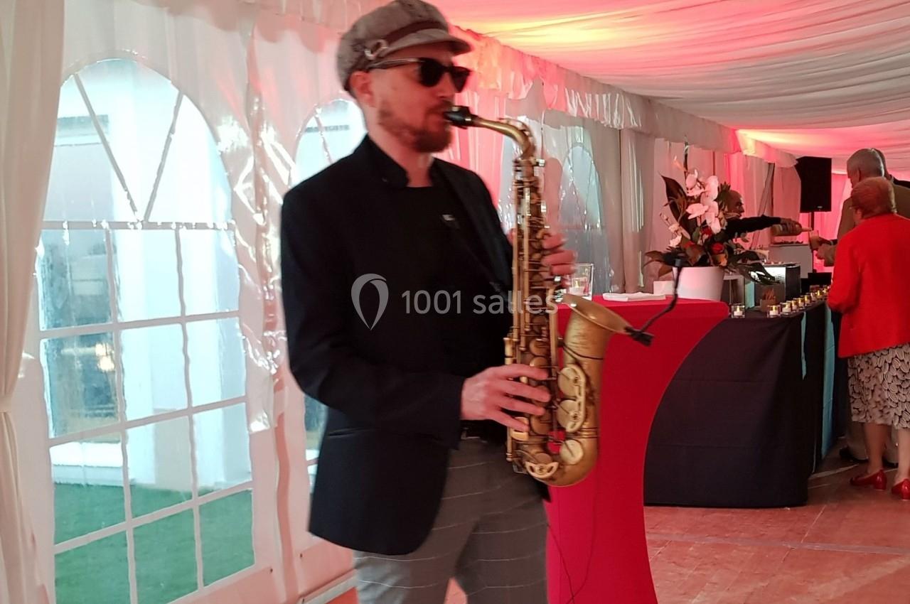 Un musicien joue du saxophone dans une salle décorée avec des lumières rouges et des tables de réception.