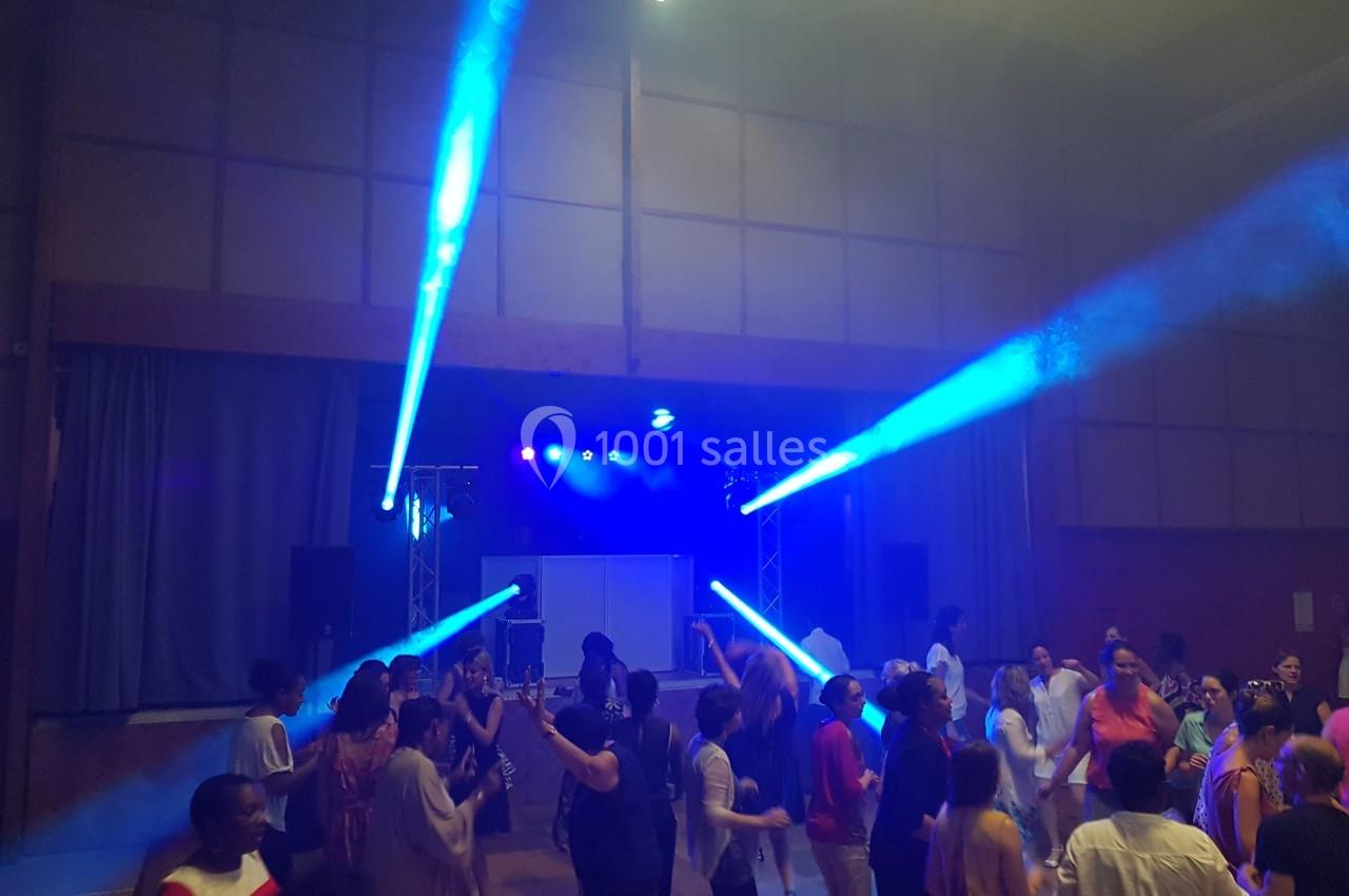 Des personnes dansent dans une salle éclairée par des projecteurs bleus, créant une ambiance festive.