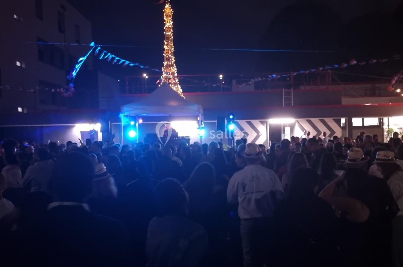 Foule rassemblée en soirée devant une scène éclairée, avec des décorations lumineuses en arrière-plan.