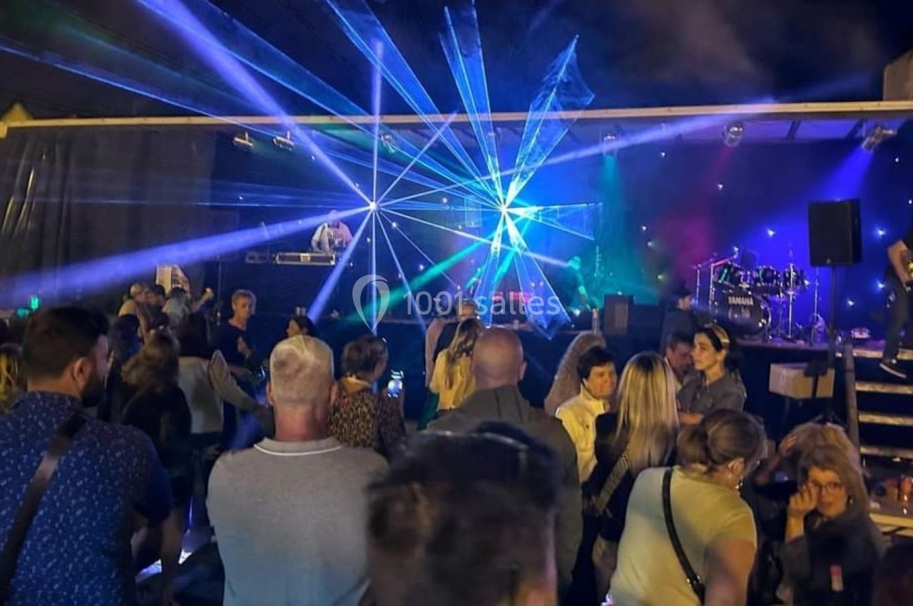 Foule rassemblée devant une scène en plein air avec jeux de lumière et musique live.