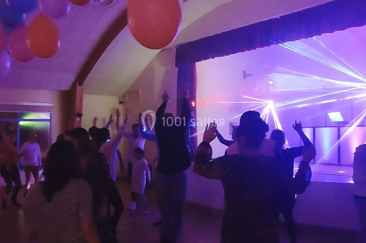 Des personnes dansent dans une salle éclairée par des lumières colorées et des lasers, avec des ballons suspendus au plafond.