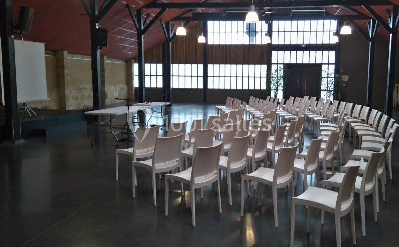 Salle de conférence lumineuse avec des rangées de chaises blanches alignées face à un écran de projection.