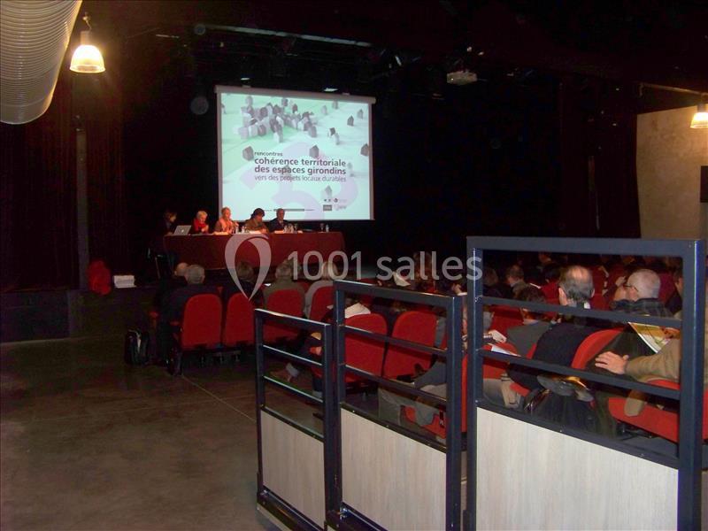 Un panel de conférenciers s'exprime devant un public assis dans une salle sombre avec un écran de projection.
