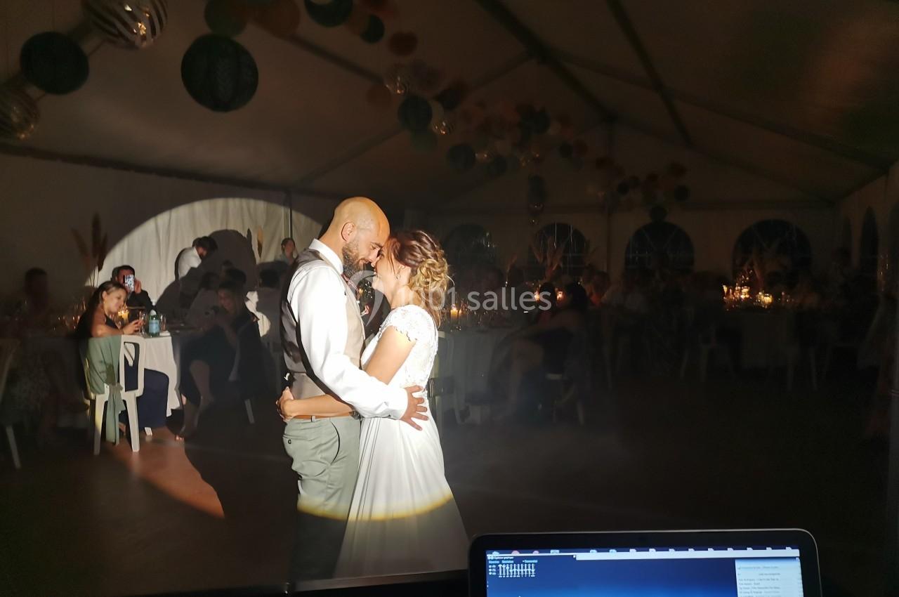 Un couple danse sous un éclairage tamisé dans une salle décorée, entouré d'invités assis à des tables.