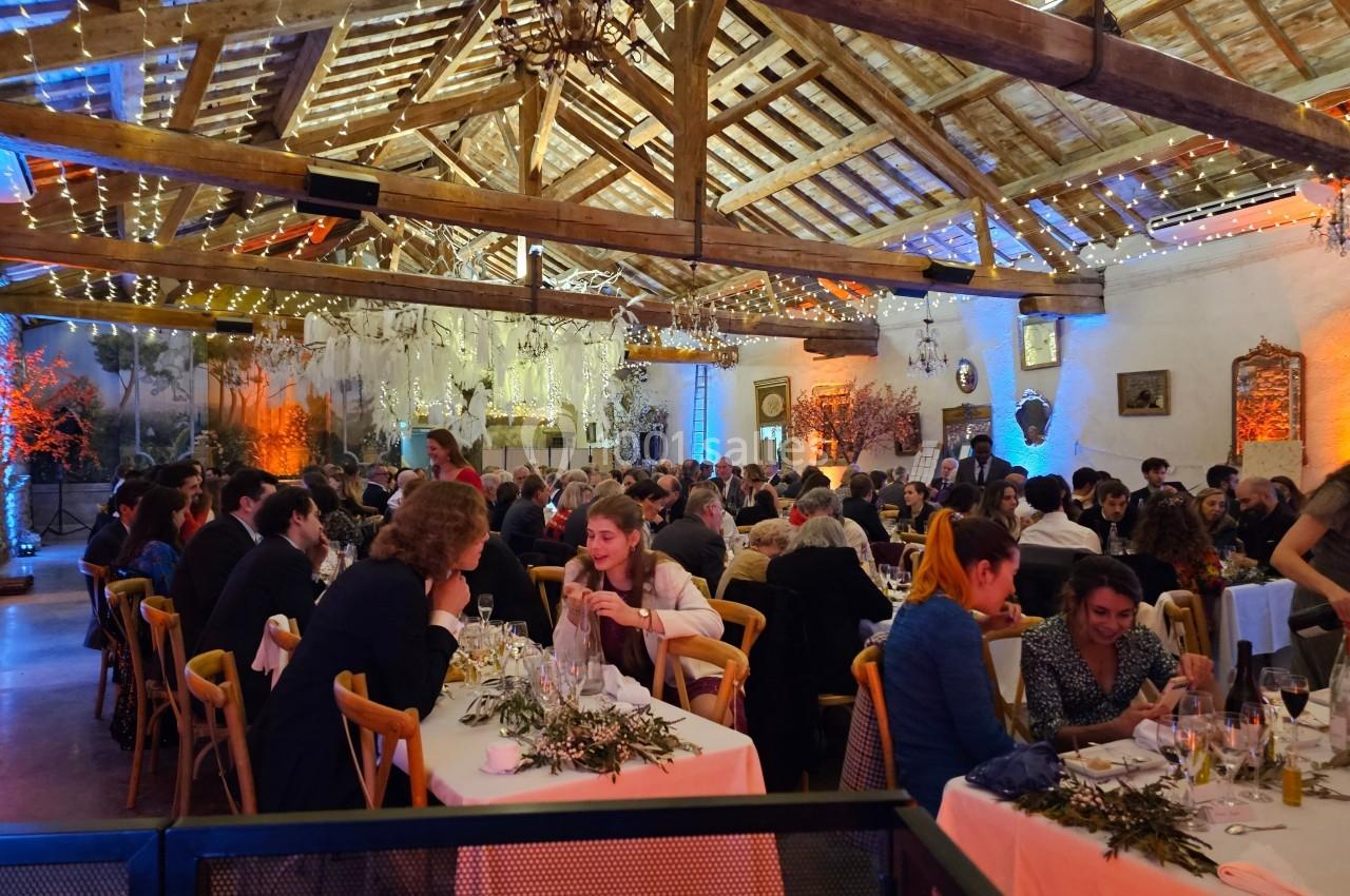 Salle de réception décorée avec des guirlandes lumineuses, accueillant des convives assis à des tables pour un dîner.