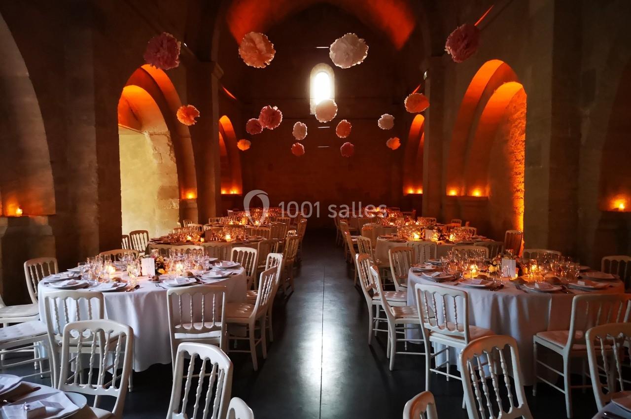 Salle voûtée éclairée par des lumières chaudes, décorée de tables rondes dressées et de suspensions florales.