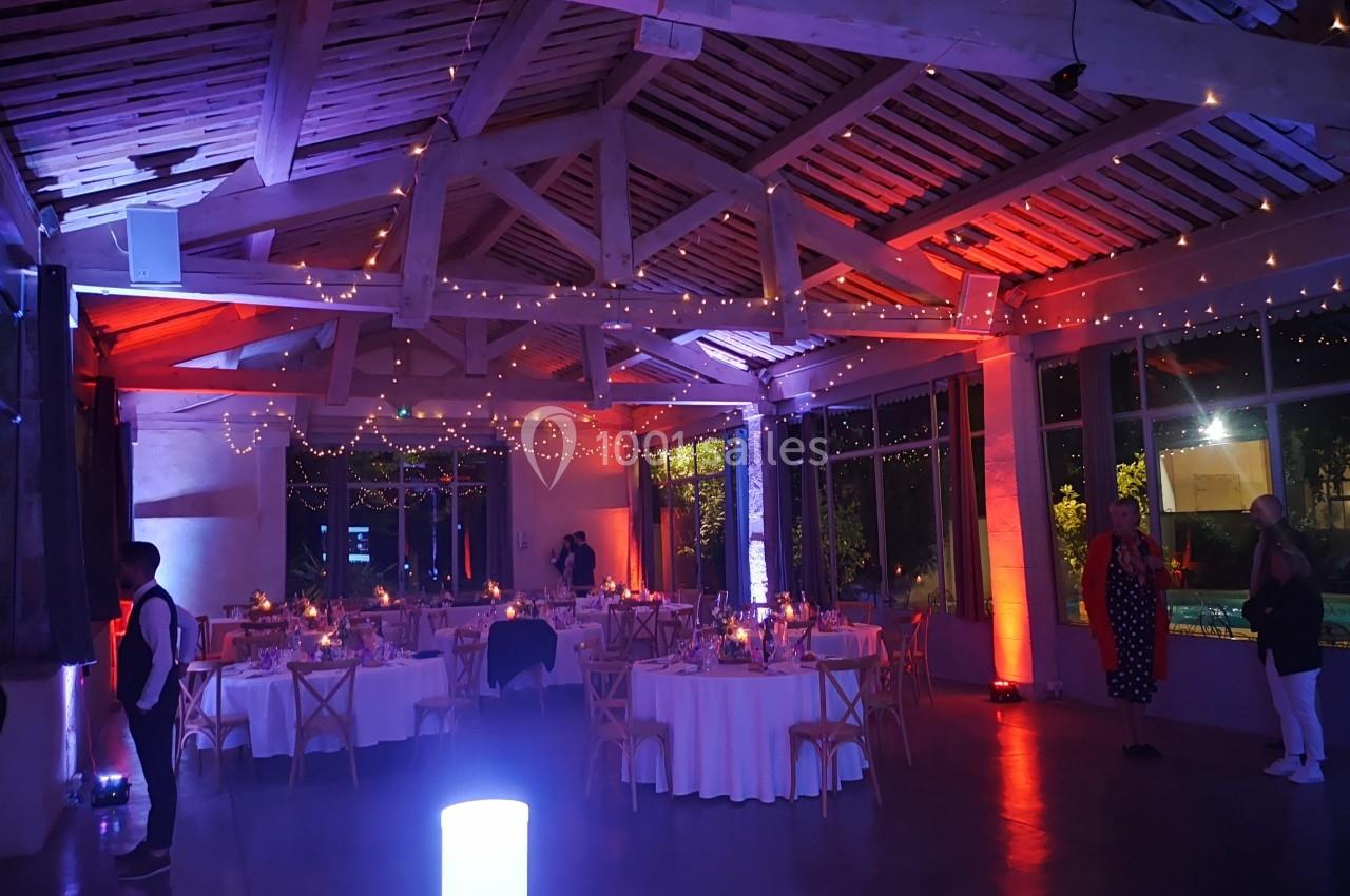 Salle de réception décorée avec des guirlandes lumineuses, tables rondes dressées et ambiance tamisée.