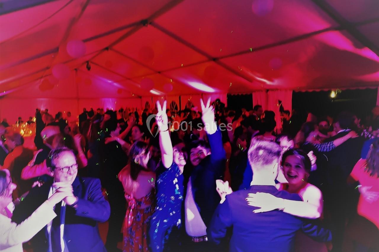 Personnes dansant sous une tente éclairée de lumières roses lors d'une fête ou d'un événement festif.