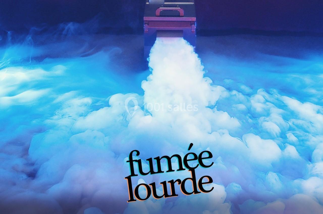 Machine diffusant une épaisse fumée blanche sur un sol éclairé par une lumière bleutée.