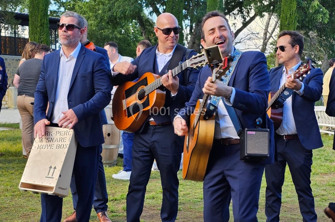 Des musiciens en costume jouent de la guitare et des percussions en plein air devant un petit groupe de personnes.