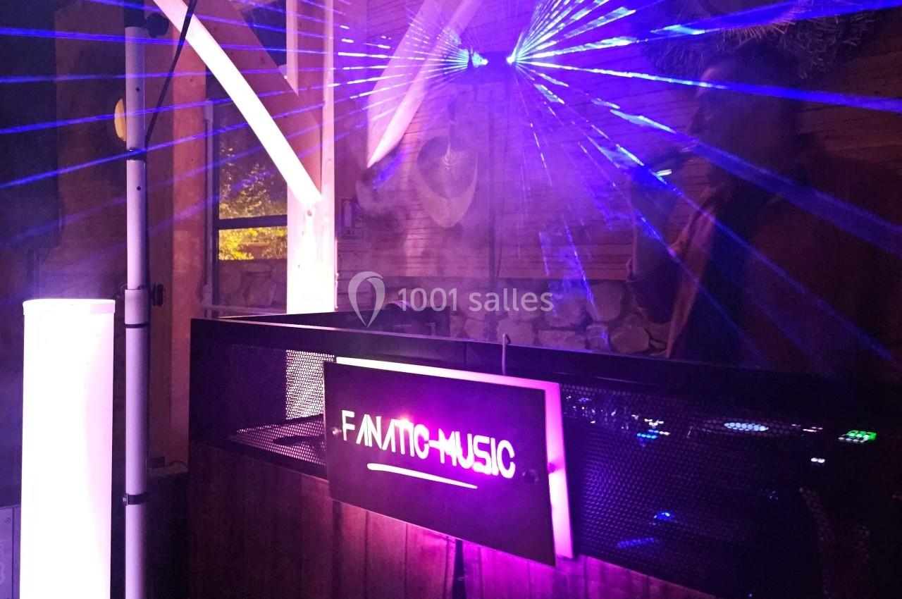 Poste de DJ éclairé par des lasers violets dans un espace intérieur avec un panneau ’F-AMIC MUSIC’.