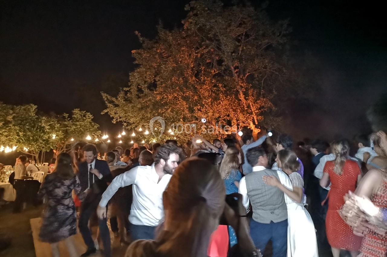 Des personnes dansent en soirée en plein air, éclairées par des guirlandes lumineuses et un arbre illuminé.