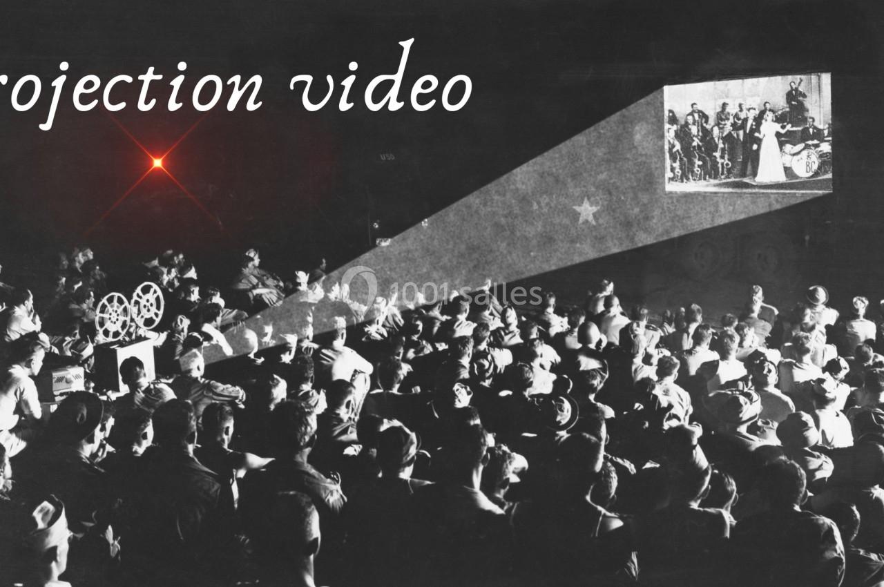 Projection d'un film en noir et blanc devant un public nombreux, avec un projecteur visible à gauche.