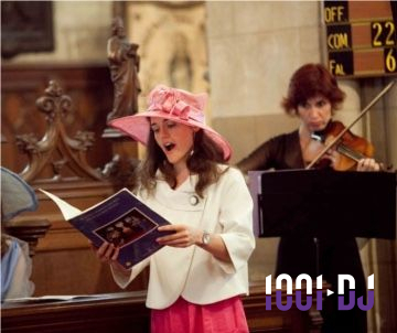 Une femme chante en lisant une partition dans une église, accompagnée par une violoniste en arrière-plan.
