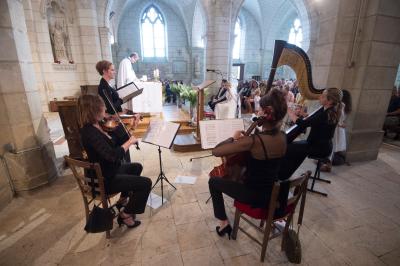 Miniature Quatuor cérémonie Une violoncelliste joue lors d'une cérémonie dans une église, entourée d'invités debout et de mariés à l'arrière-plan.
