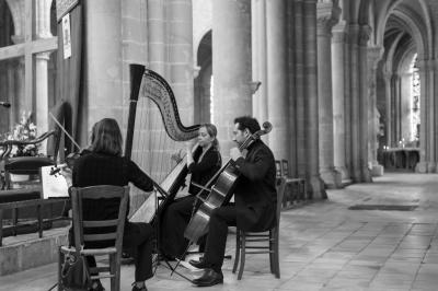 Miniature Cérémonie Trio Une violoncelliste joue lors d'une cérémonie dans une église, entourée d'invités debout et de mariés à l'arrière-plan.