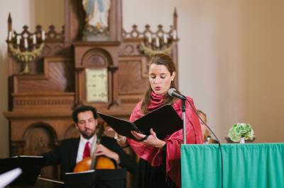 Miniature Chanteuse cérémonie Une violoncelliste joue lors d'une cérémonie dans une église, entourée d'invités debout et de mariés à l'arrière-plan.