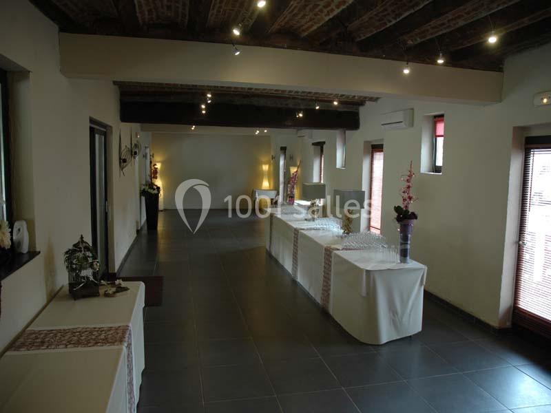 Salle lumineuse avec tables dressées, nappes blanches et décorations florales, sous un plafond en poutres apparentes.