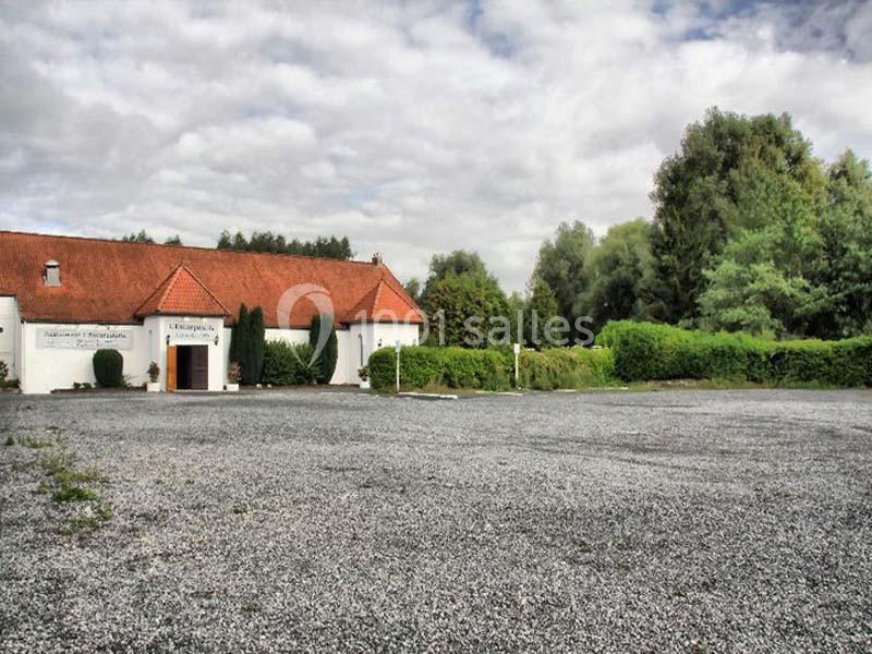 Bâtiment blanc avec toit en tuiles rouges entouré de végétation, devant une grande cour en gravier.