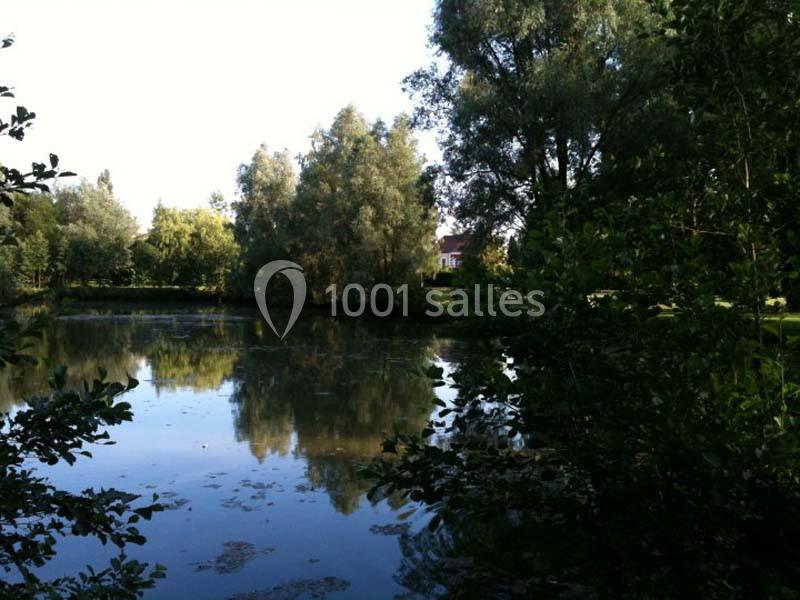 Étang entouré d'arbres et de végétation, reflétant le ciel et les feuillages dans une lumière naturelle.