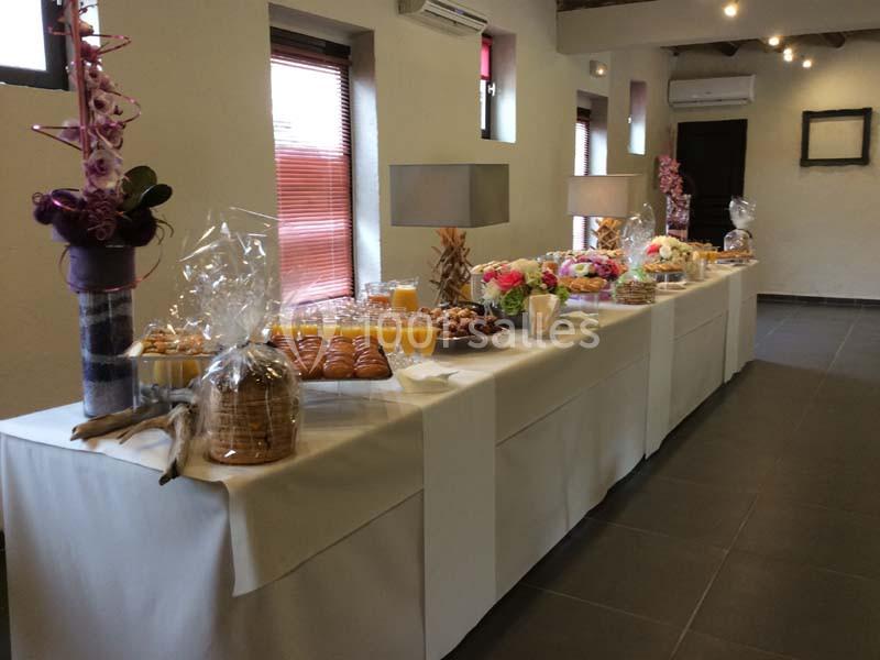 Table de buffet garnie de viennoiseries, fruits, boissons et décorations florales dans une salle lumineuse.