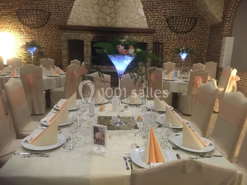Salle de réception décorée avec des tables élégantes, nappes blanches, serviettes pliées et centre de table lumineux.
