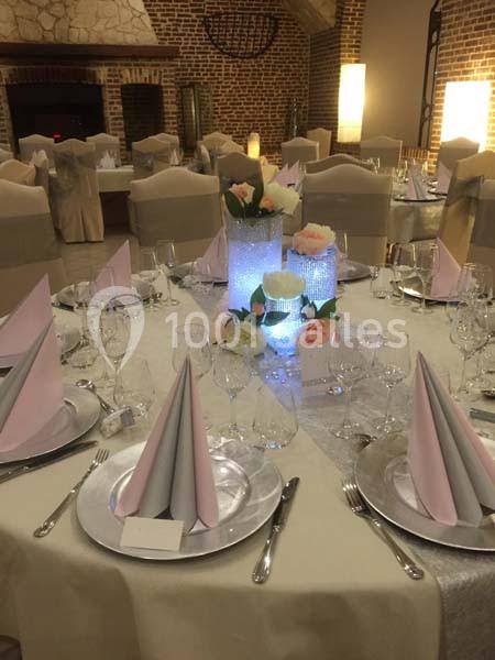 Table élégamment dressée avec nappes blanches, serviettes pliées, vaisselle raffinée et centre de table floral lumineux.