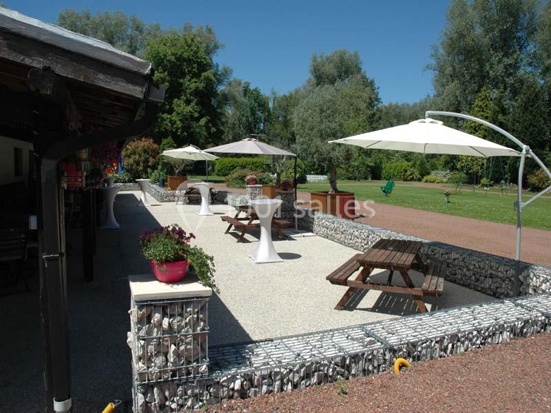 Terrasse aménagée avec tables en bois, parasols et jardinières, entourée de verdure et d'arbres.