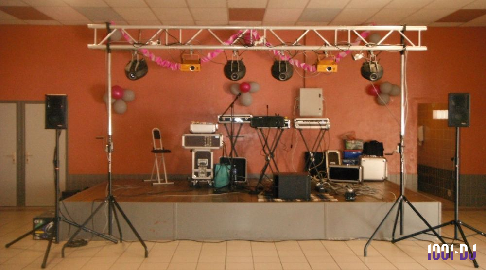 Matériel de sonorisation et éclairage installé sur une petite scène dans une salle aux murs orange.