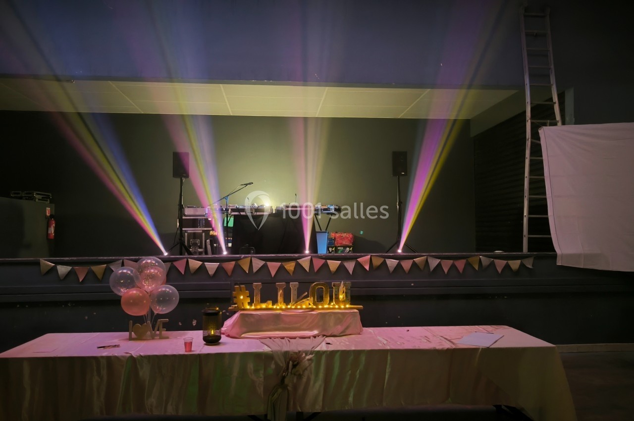 Scène décorée avec des lumières colorées, une table ornée de ballons et un panneau lumineux ’ALOHA’.