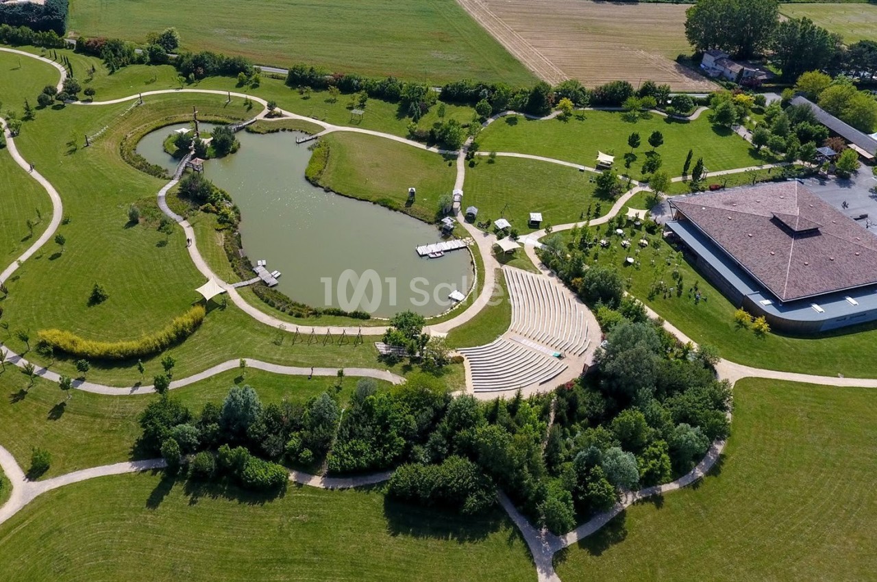 Vue aérienne d'un parc avec un étang, des chemins sinueux, un amphithéâtre en plein air et un bâtiment adjacent.