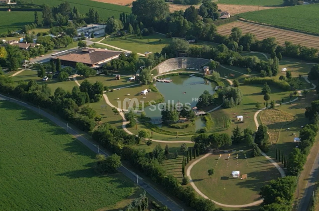 Vue aérienne d'un parc verdoyant avec un lac central, des chemins sinueux et des bâtiments entourés de champs.