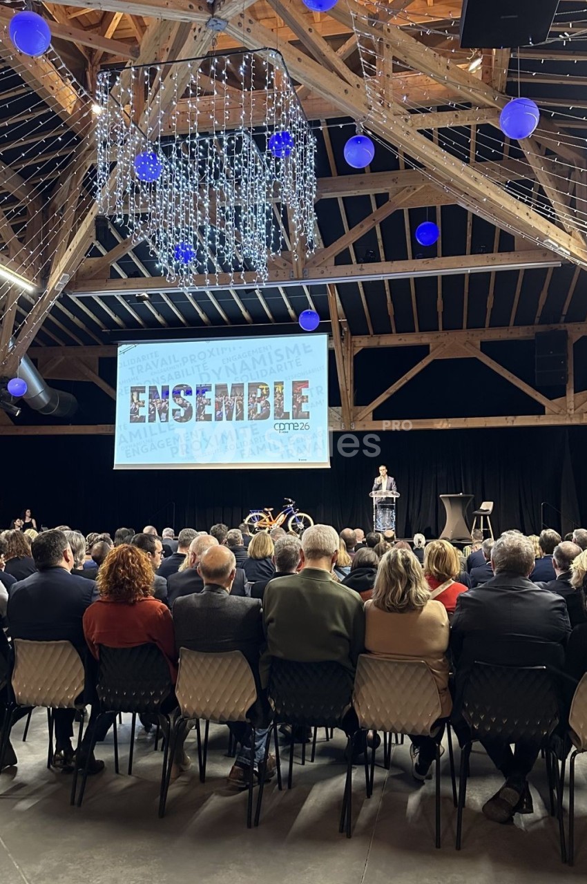 Salle de conférence avec un public assis, un orateur sur scène et un écran affichant le mot ’ENSEMBLE’.