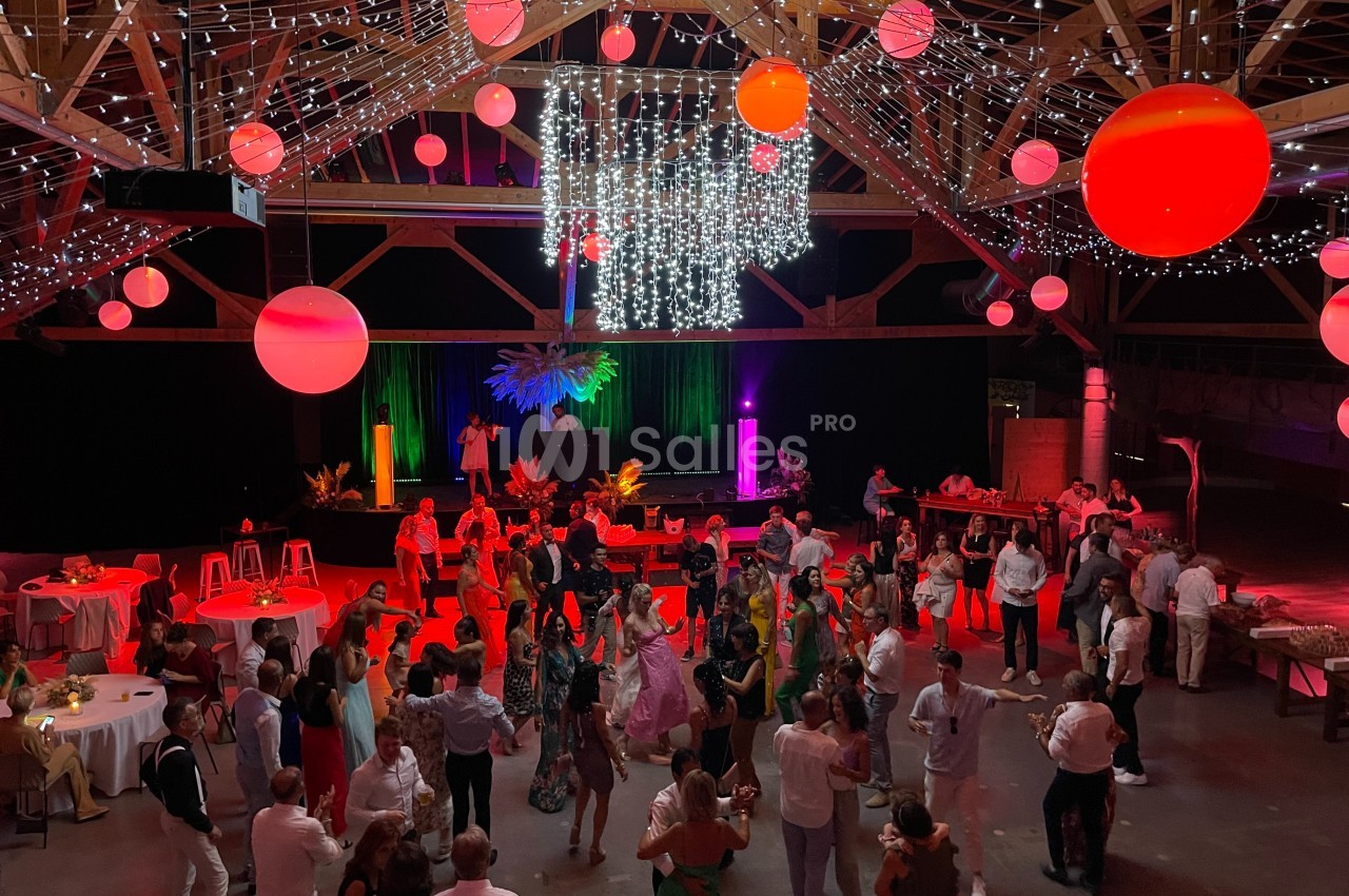 Salle décorée avec des guirlandes lumineuses et des lanternes rouges, des invités dansent sur une piste éclairée.