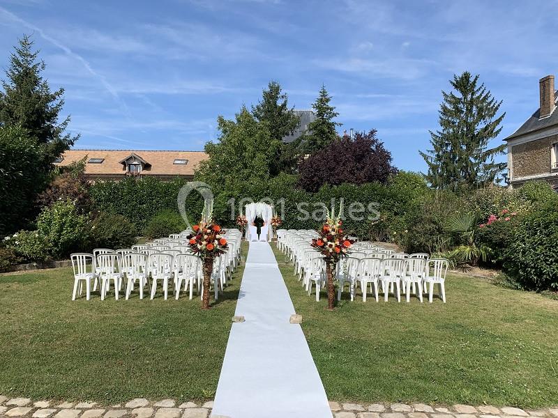 Allée centrale bordée de chaises blanches et décorations florales, menant à une arche de mariage en plein air.