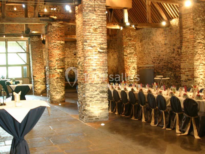 Location salle Court-Saint-Étienne (Brabant wallon) - Ferme de Beaurieux #2 Salle en pierre avec poutres apparentes, tables dressées pour un événement et lumière naturelle entrant par une grande baie…