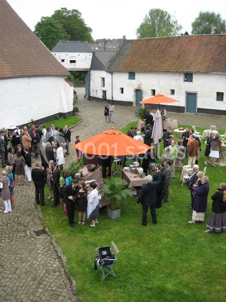 Location salle Court-Saint-Étienne (Brabant wallon) - Ferme de Beaurieux #17 Groupe de personnes rassemblées dans une cour pavée entourée de bâtiments anciens, avec des parasols orange.