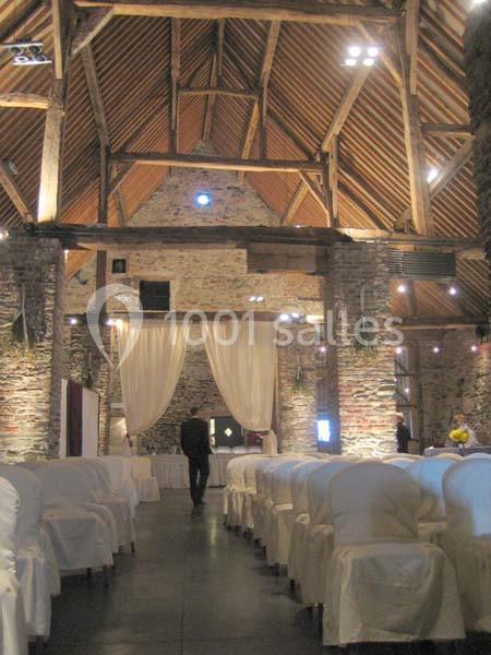Location salle Court-Saint-Étienne (Brabant wallon) - Ferme de Beaurieux #19 Salle en pierre avec poutres apparentes, rangées de chaises blanches et rideaux clairs au fond.