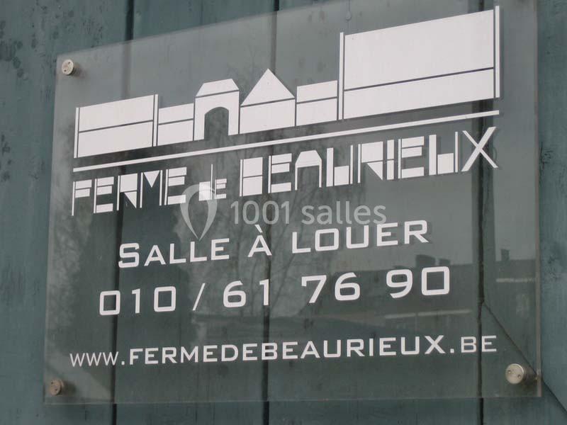 Location salle Court-Saint-Étienne (Brabant wallon) - Ferme de Beaurieux #8 Panneau transparent indiquant ’Ferme de Beaurieux’, avec contact pour location de salle et site web mentionné.