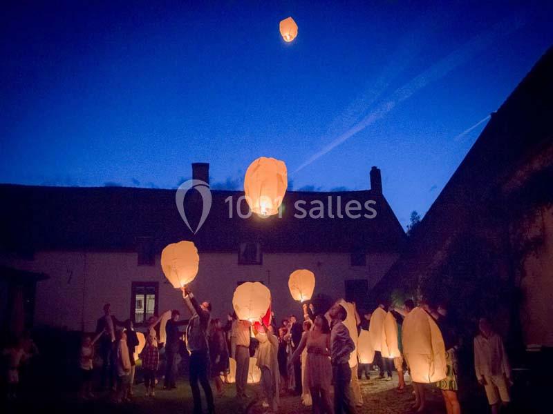 Location salle Court-Saint-Étienne (Brabant wallon) - Ferme de Beaurieux #10 Des personnes rassemblées la nuit lancent des lanternes volantes illuminées dans un ciel sombre.