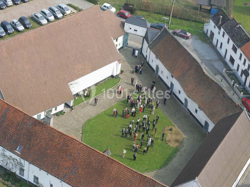 Location salle Court-Saint-Étienne (Brabant wallon) - Ferme de Beaurieux #11 Vue aérienne d'une cour intérieure entourée de bâtiments avec un rassemblement de personnes au centre.