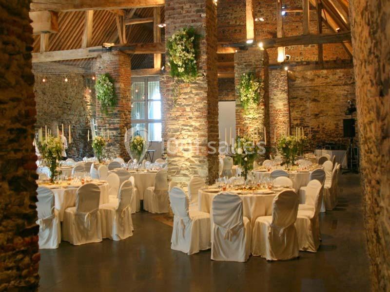 Location salle Court-Saint-Étienne (Brabant wallon) - Ferme de Beaurieux #4 Salle de réception en pierre avec tables rondes décorées, chaises blanches et arrangements floraux suspendus.
