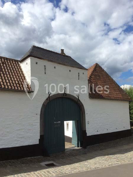 Location salle Court-Saint-Étienne (Brabant wallon) - Ferme de Beaurieux #20 Façade d'un bâtiment ancien en briques blanches avec une grande porte cochère en bois vert et un toit en tuiles.