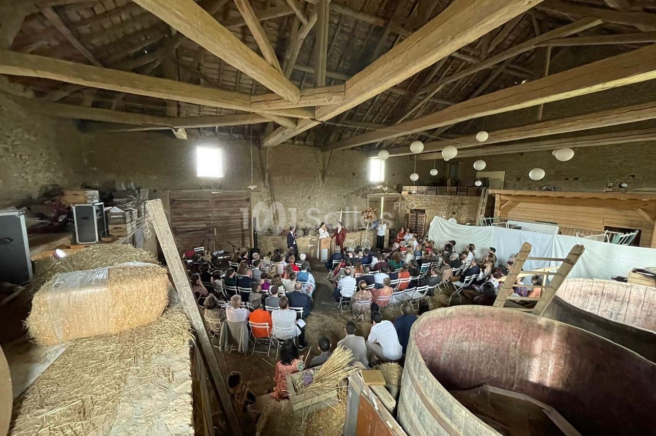 Un groupe de personnes assises dans une grange en bois, assistent à une présentation ou un spectacle.