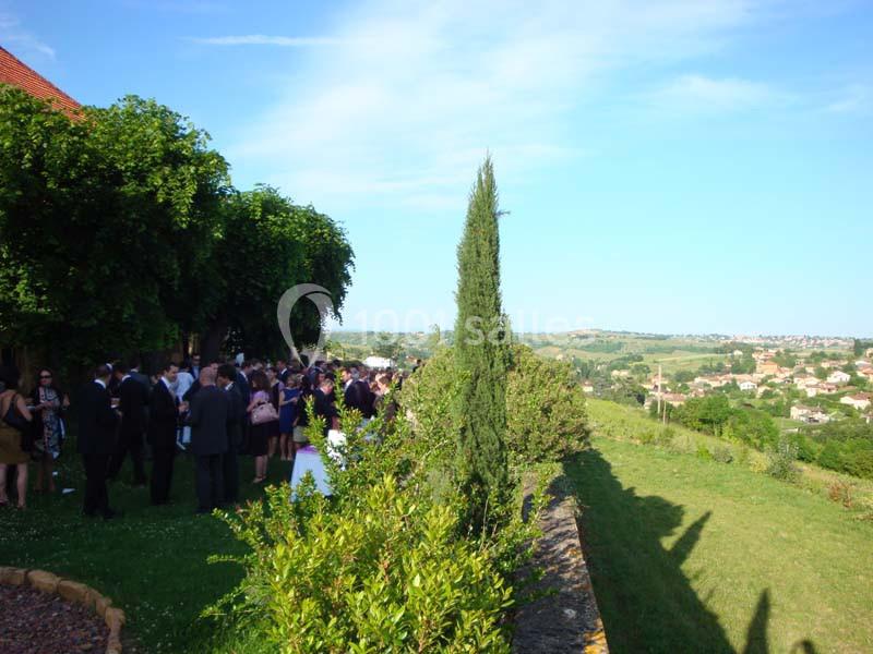 Groupe de personnes rassemblées dans un jardin verdoyant avec vue sur une campagne vallonnée sous un ciel dégagé.